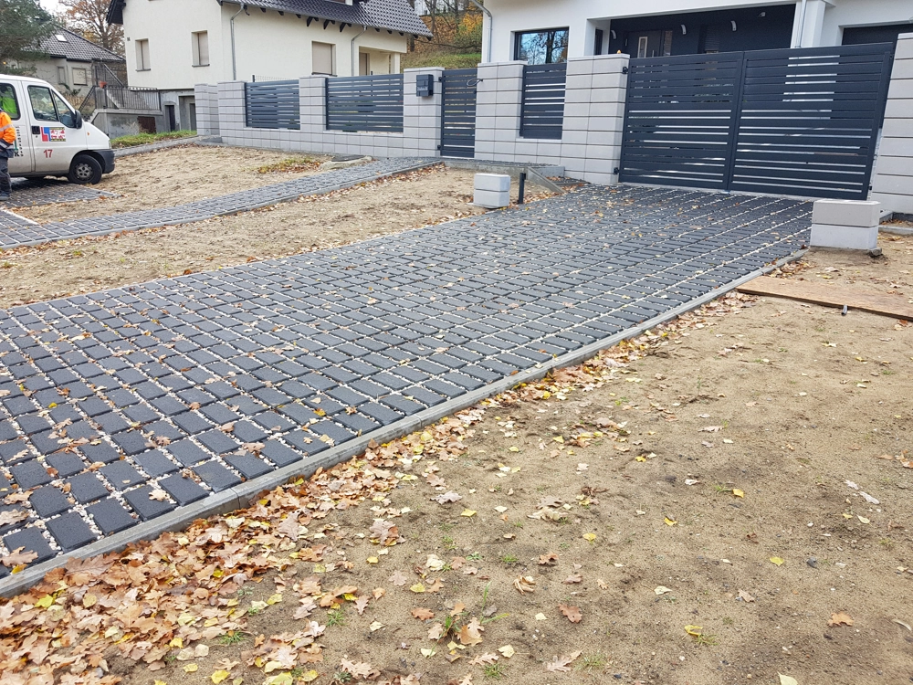 Układanie kostki brukowej ażurowej na podjeździe przy nowoczesnym ogrodzeniu