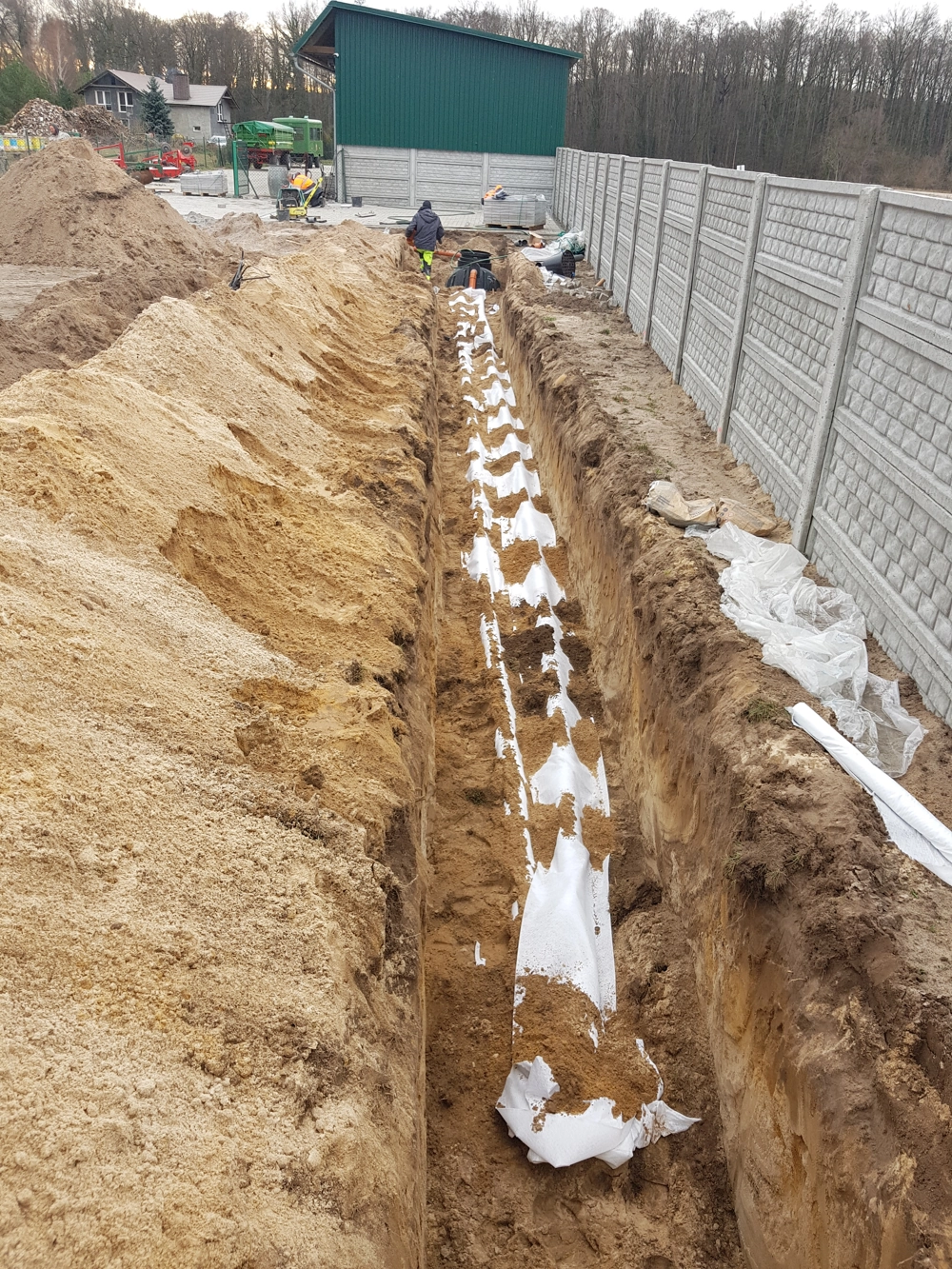 Drenaż opaskowy w wykopie przy betonowym ogrodzeniu z geowłókniną i rurą drenażową