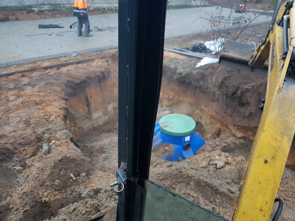Wykop pod zbiornik na deszczówkę wykonany minikoparką, widoczny niebieski zbiornik z zielonym włazem
