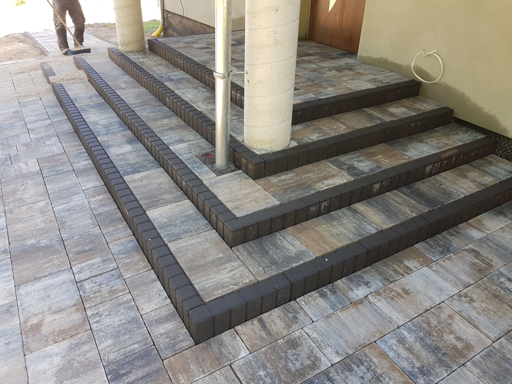 Wielopoziomowe schody z kostki brukowej z ciemnymi krawężnikami przy elewacji budynku