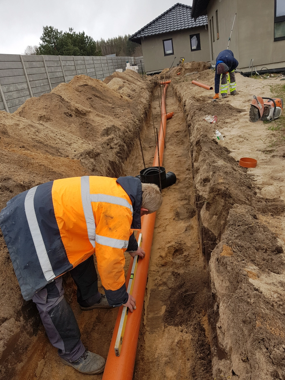 Drenaż w wykopie przy budynku – układanie rur odprowadzających wodę