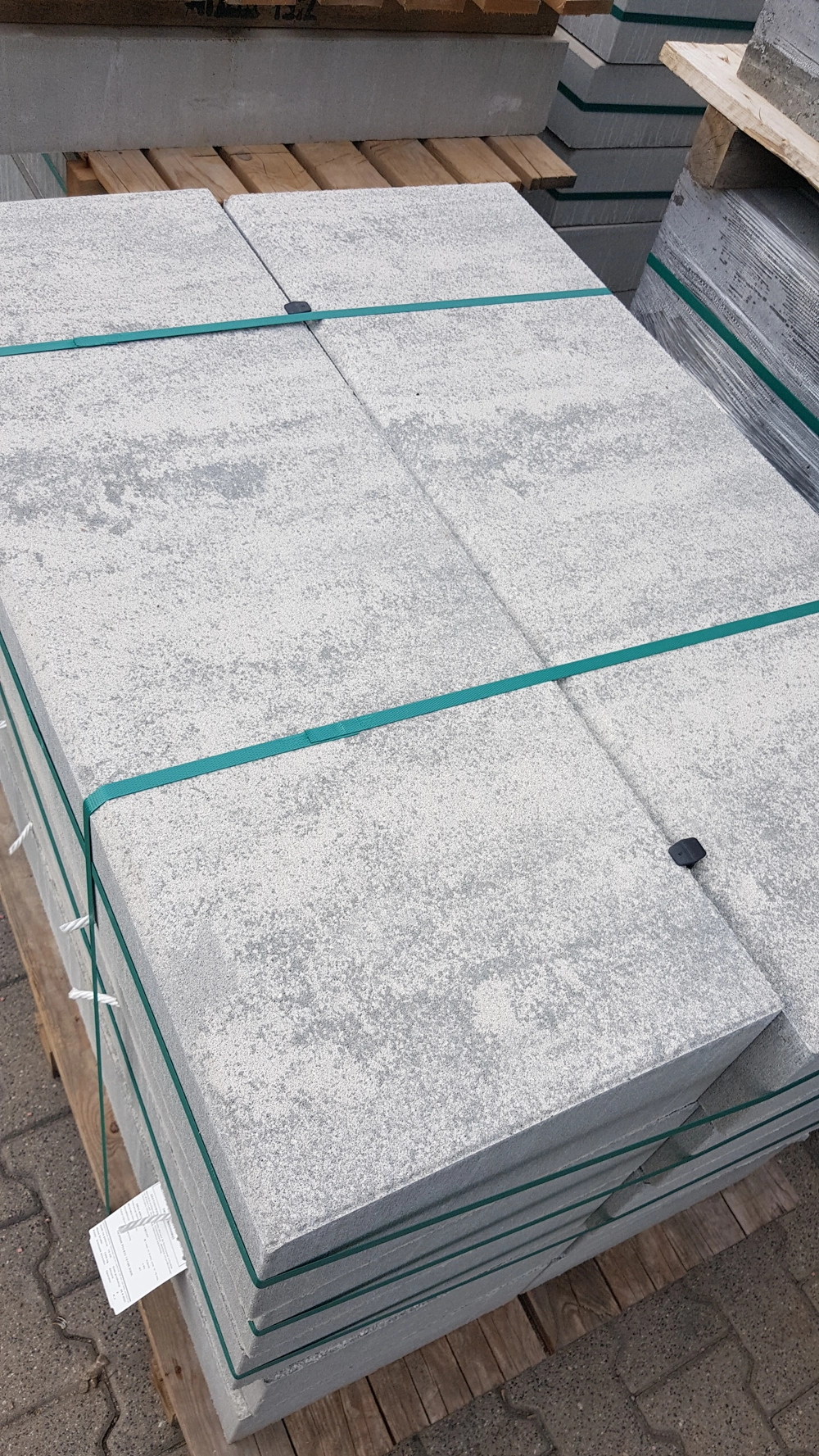 Płyty tarasowe betonowe w stosie na palecie zabezpieczone taśmami, gotowe do układania