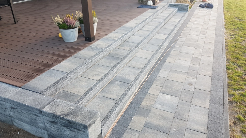 Schody z kostki brukowej: dwa stopnie wykonane z szarej kostki przy tarasie z donicami
