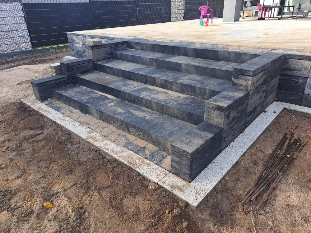 Schody z kostki brukowej z ciemnoszarych bloczków prowadzące na taras z białą opaską