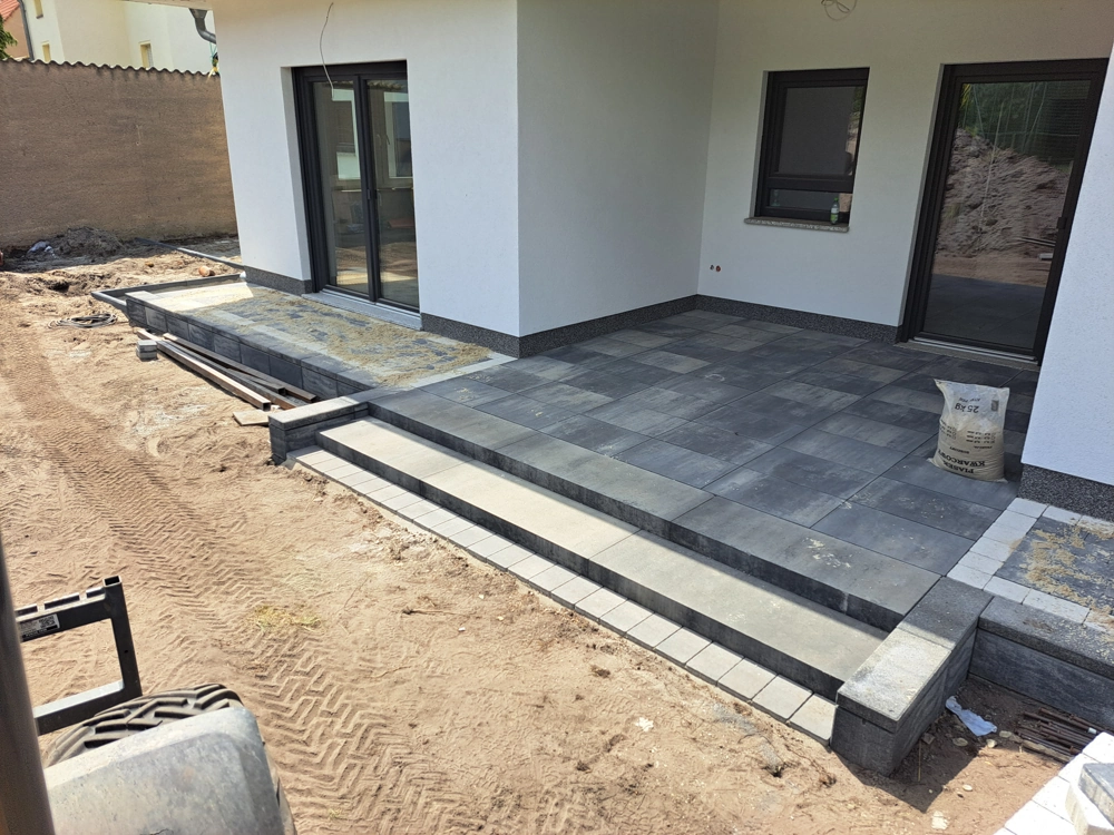 Taras przed domem wyłożony płytami tarasowymi betonowymi z dwustopniowymi schodami