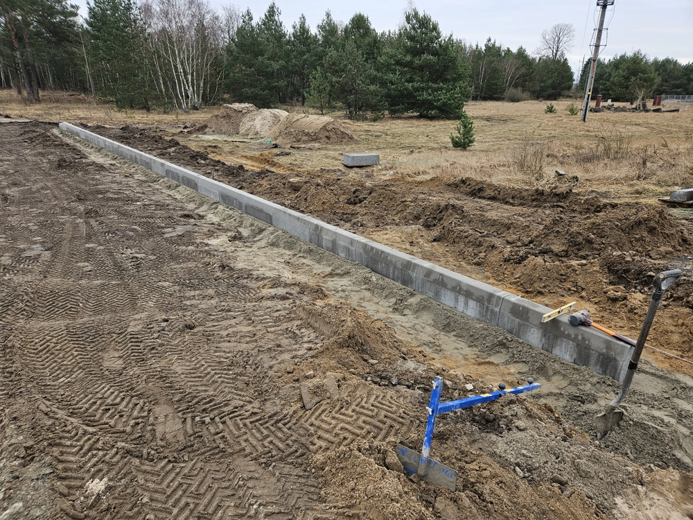 Rząd betonowych krawężników ułożonych w wykopie na wyrównanym gruncie
