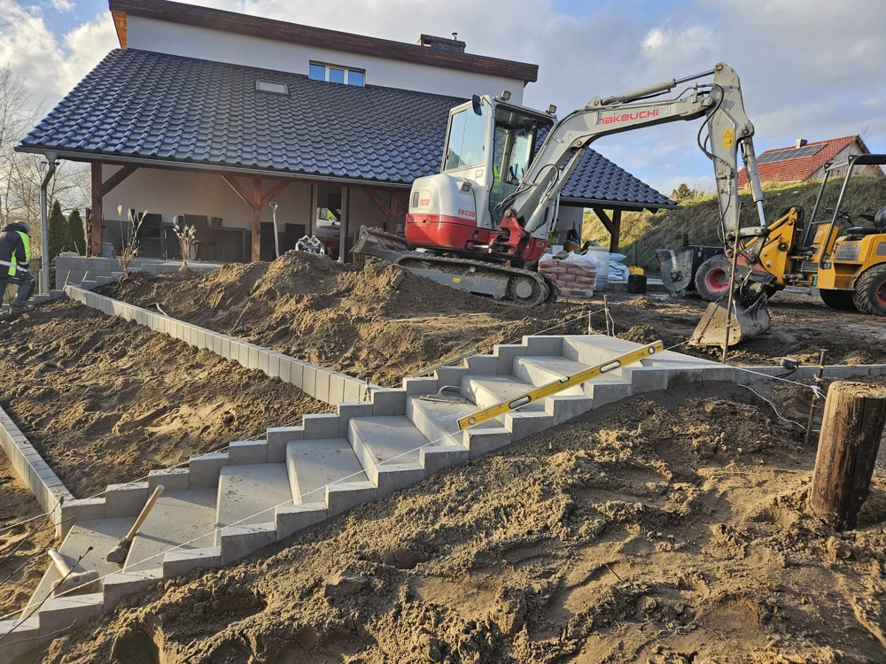 Schody betonowe montowane na pochyłym nasypie z użyciem minikoparki