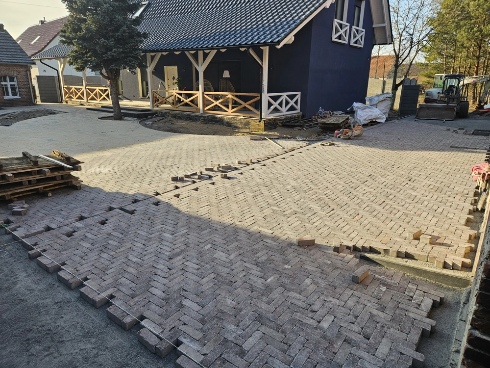 Układanie kostki brukowej w jodełkę na podjeździe przed budynkiem mieszkalnym, przygotowany podkład piaskowy