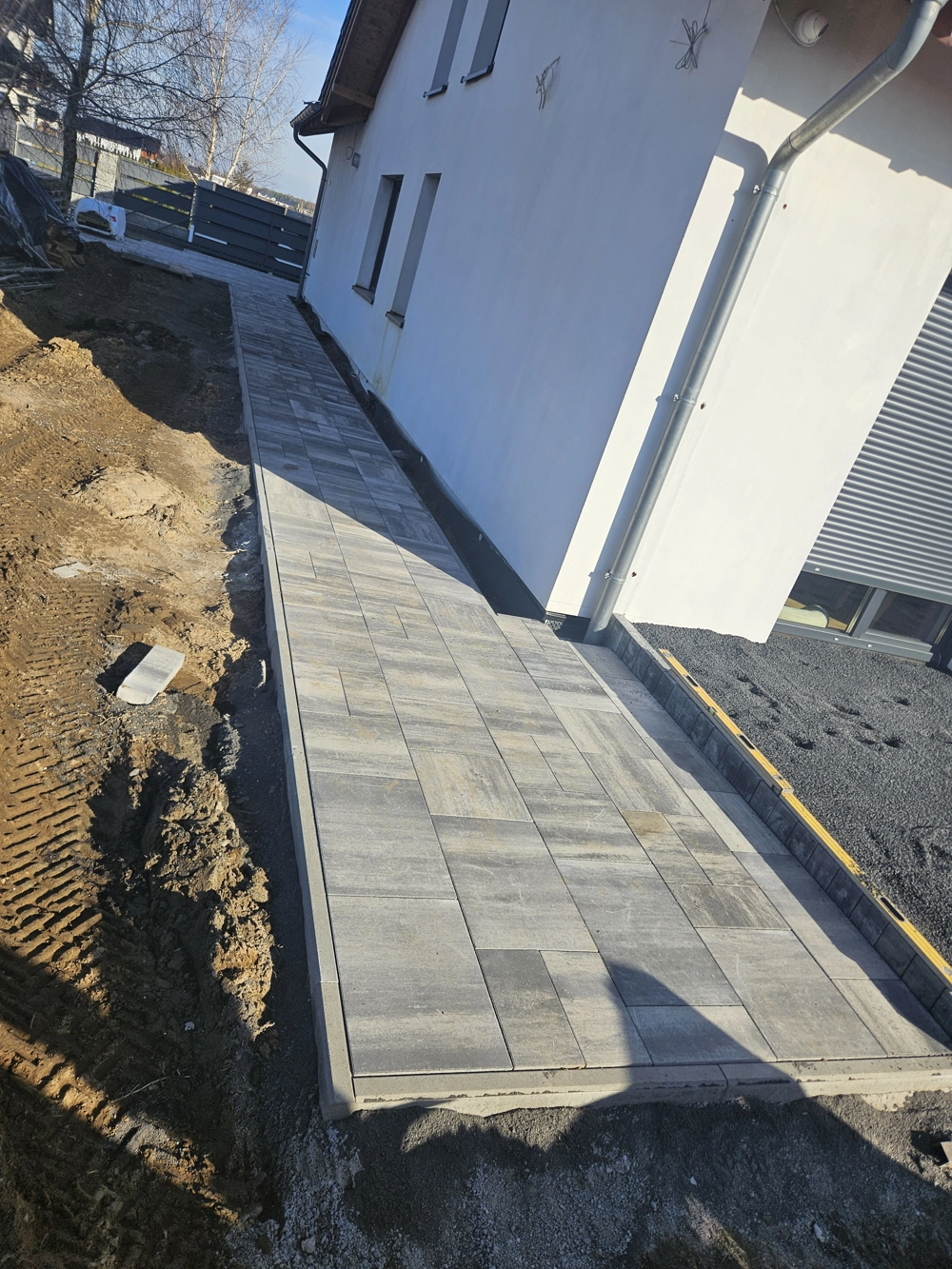 Opaska wokół domu z kostki brukowej ułożona przy białej elewacji