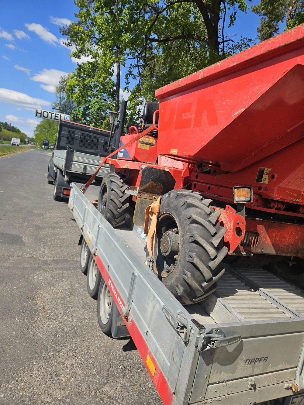 Wozidło budowlane przewożone na przyczepie transportowej przy drodze