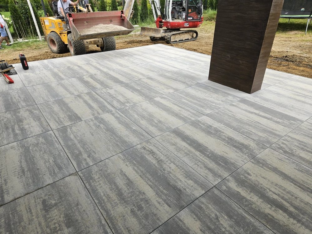 Układanie płyt tarasowych betonowych na wyrównanym podłożu z ładowarką kołową w tle