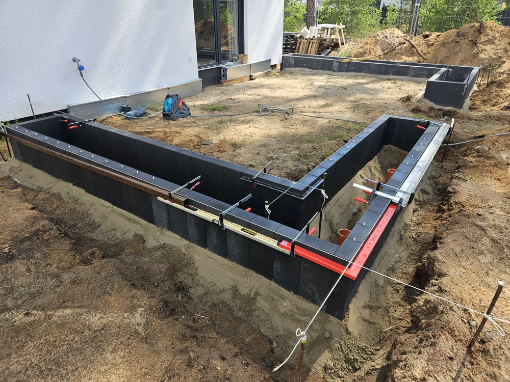 Prace ziemne: montaż czarnych bloczków formowych pod fundament przy domu