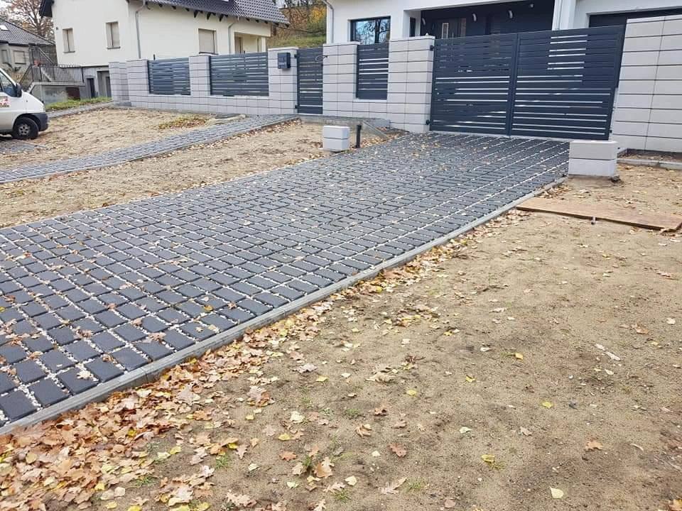 Układanie kostki brukowej w formie ażurowych kratek na podjeździe przy nowoczesnym betonowym ogrodzeniu