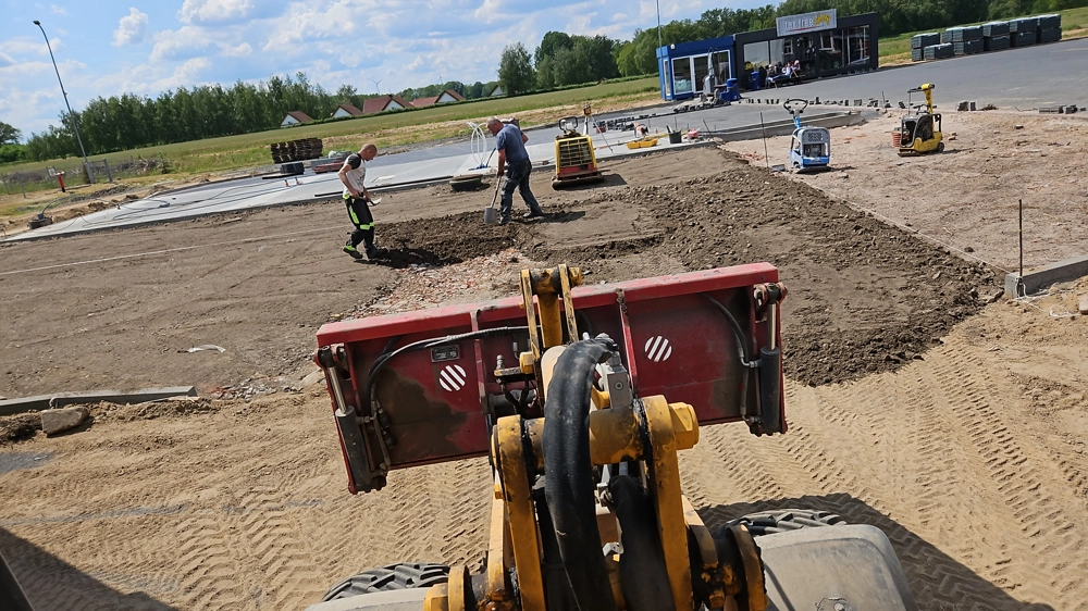 Niwelacja terenu z użyciem ładowarki kołowej i pracowników przygotowujących podłoże pod układanie kostki