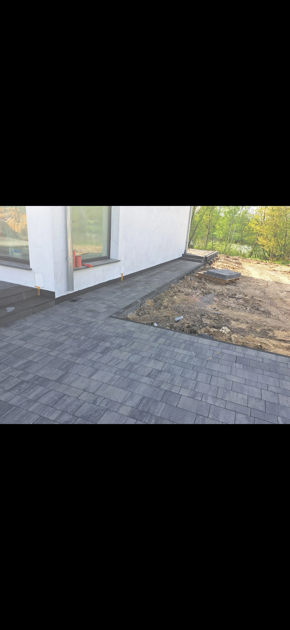 Opaska wokół domu z kostki brukowej w szarym kolorze ułożona przy elewacji budynku z dużym przeszkleniem