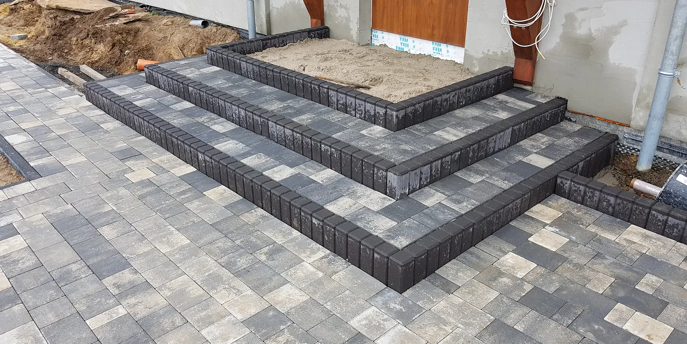 Trójstopniowe schody z kostki brukowej w odcieniach szarości na podwórku przy budynku