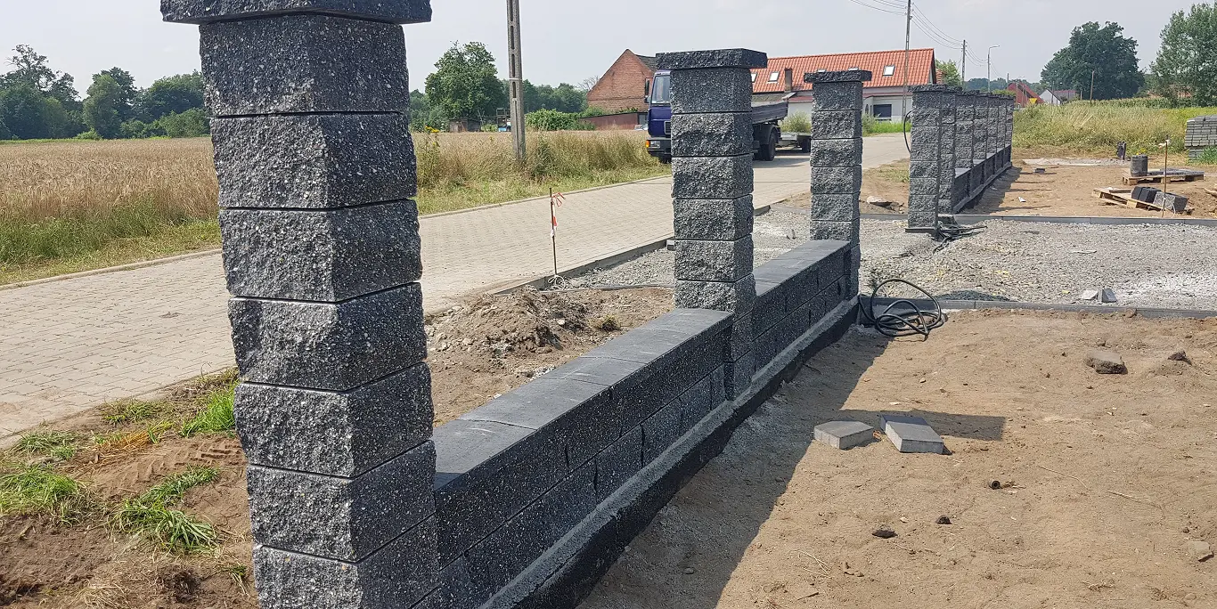 Betonowe słupki i niski mur z prefabrykowanych bloczków w trakcie montażu ogrodzenia betonowego