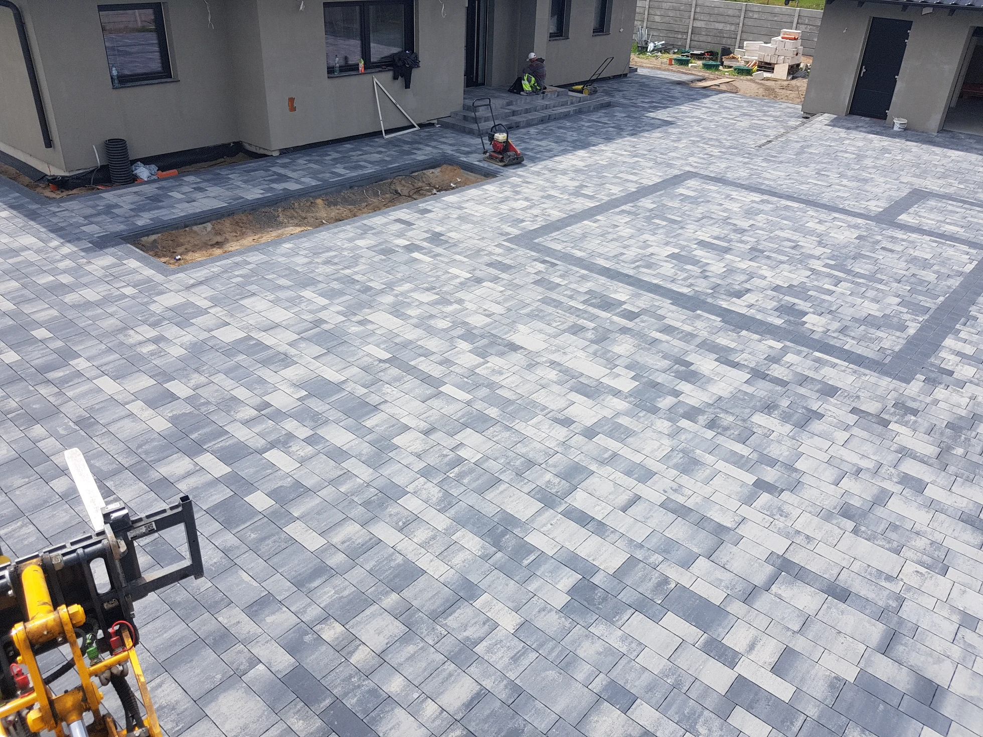 Układanie kostki brukowej na podjeździe – równomierne szaro-białe betonowe kostki brukowe przy domu